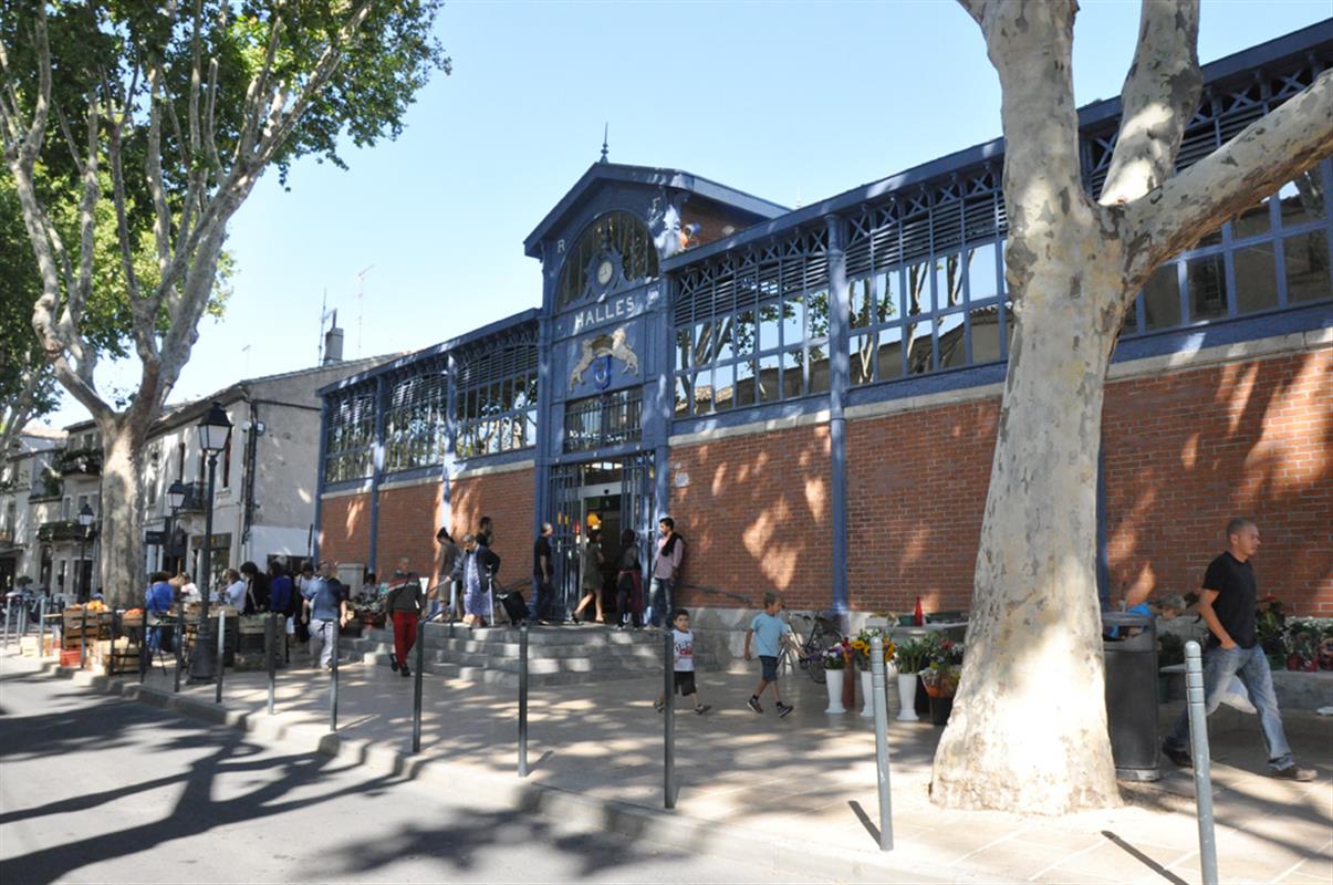 Les halles de Lunel, façade bleue, arbres au premier plan et passage de piétons